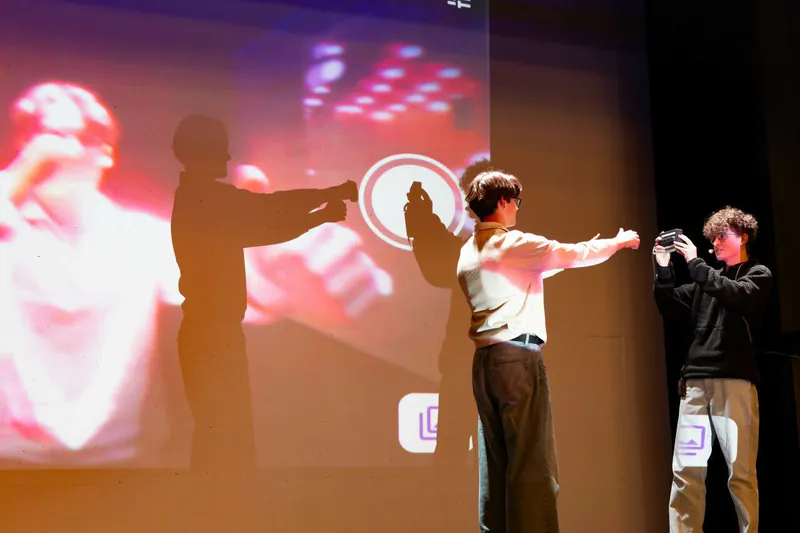 On stage, the founder photographs a volunteer with the camera while the capture screen is projected behind them.